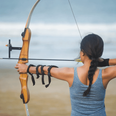 "Vrouw beoefent boogschieten op het strand, geïnspireerd door Robin Hood, genietend van een uniek avontuur met vrienden of familie