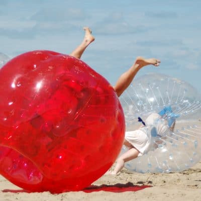 Mensen spelen botsvoetbal op het strand met bubbelballen, vol actie en plezier in de buitenluc