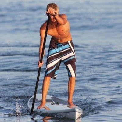 Man staat op een Stand Up Paddle Board en peddelt op de zee, genietend van het suppen op het wate
