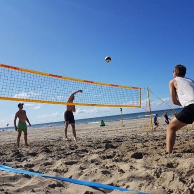 Mensen spelen beachvolleybal op het strand, omringd door zand, zee en blauwe lucht, genietend van een zonnige dag