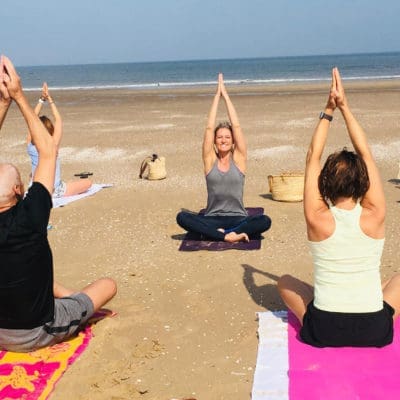 "Mensen beoefenen yoga op het strand, omringd door de zee en duinen, ervaren innerlijke rust en harmoniev