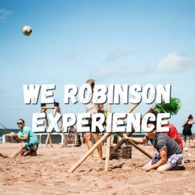 Een groep mensen op het strand versterkt hun teamband met een intens touwtrekwedstrijd, passend bij de We Robinson Experience. Dit avontuur vol teamwork speelt zich af On The Beach, waar deelnemers strijden en plezier hebben