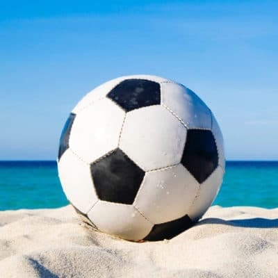 Mensen spelen beachvoetbal op het strand, omringd door zand en de zee, terwijl ze genieten van een leuke en actieve dag
