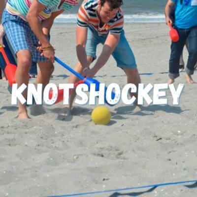 Mensen spelen Knotshockey op het strand, genietend van het gekke spel met reuze wattensticks en teamspirit