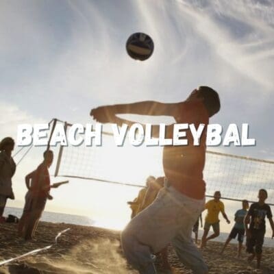 Mensen spelen beachvolleybal op het strand, omringd door zand, zee en blauwe lucht, genietend van een zonnige dag